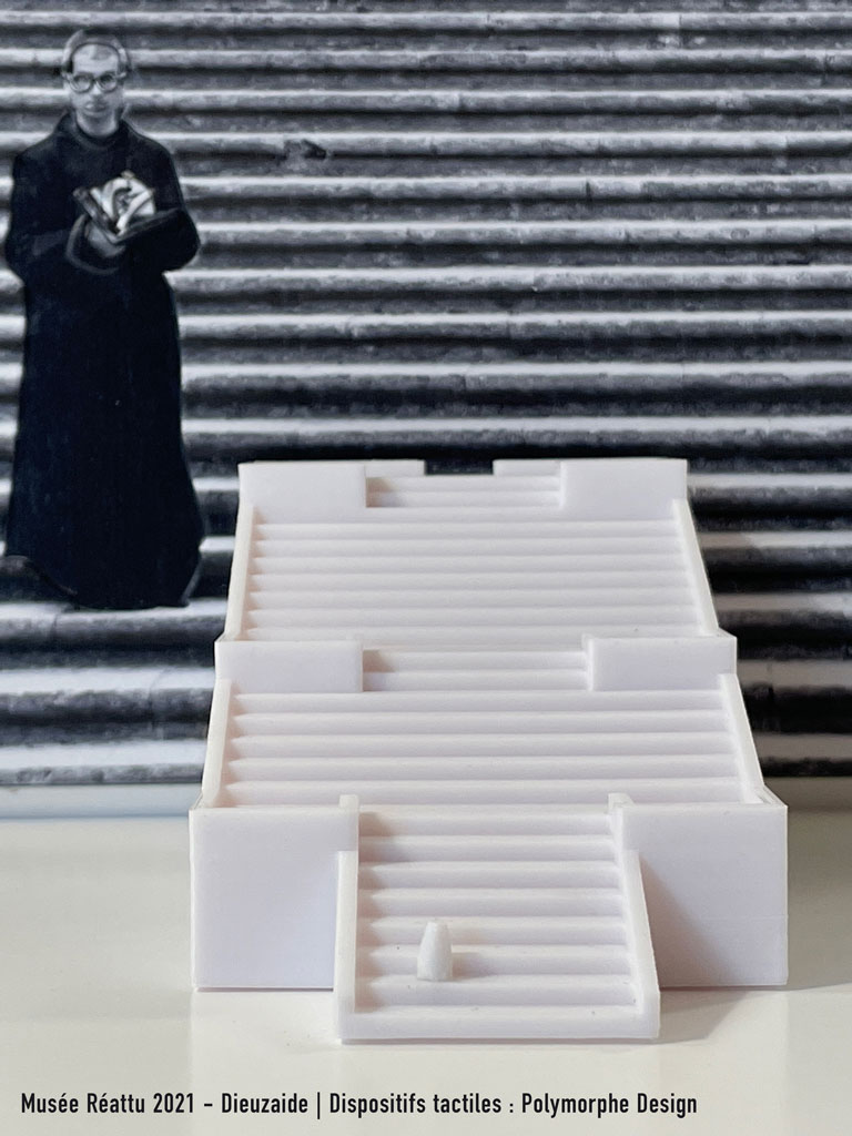 Au premier plan se trouve la maquette 3D de l'escalier de Gérone. En arrière plan, la photographie de Dieuzaide remplit l'image de ses lignes horizontales. L'ecclésiastique apparait sur la gauche de l'image.